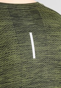 Grönmönstrad träningsskjorta med en texturerad tyg, rund halsringning och en reflekterande vit detalj på baksidan.