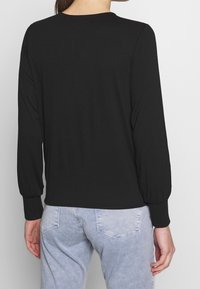 Haut noir à manches longues avec un col arrondi et des manches bouffantes, fabriqué dans un matériau doux. Associé à un pantalon en denim bleu clair.