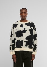 Sweter z teksturowanej wełny w czarno-białą krówkową wzór, okrągły dekolt i prążkowane mankiety. Luźny krój z miękkiego, ciepłego materiału.