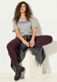 Grijze t-shirt met paarse "1987" print, gecombineerd met bordeauxrode broek en zwarte chunky enkellaarzen. Gestyled met een grijze spijkerjack.