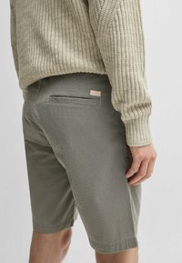 Shorts grigi a fantasia realizzati in un tessuto testurizzato, con una singola tasca posteriore e un piccolo tag con logo color crema. Stile casual.