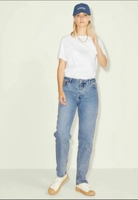T-shirt branca, jeans azuis e ténis brancos com solas de borracha. Um boné azul está utilizado. Design simples com um corte descontraído e perna reta.