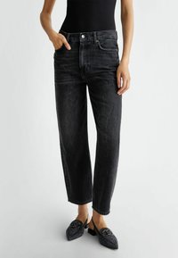 Jeans de mezclilla negros con corte relajado, que cuentan con un diseño de cinco bolsillos y un cierre de botón. Combinados con unos zapatos negros de lona texturizados sin cordones.