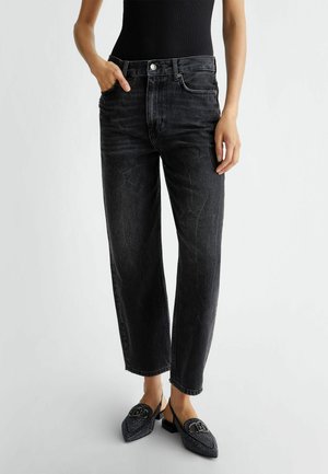 Jeans de mezclilla negros con corte relajado, que cuentan con un diseño de cinco bolsillos y un cierre de botón. Combinados con unos zapatos negros de lona texturizados sin cordones.