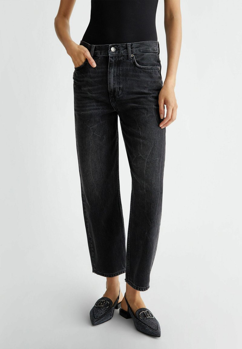 Jeans de mezclilla negros con corte relajado, que cuentan con un diseño de cinco bolsillos y un cierre de botón. Combinados con unos zapatos negros de lona texturizados sin cordones.