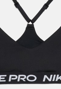 Μαύρο αθλητικό σουτιέν Nike Pro με ρυθμιζόμενους λουριά σε σχήμα σταυρού και ελαστική ταινία με λευκή στάμπα Nike Pro.