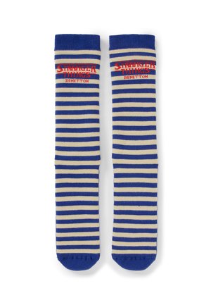 Niebiesko-kremowe podkolanówki w paski z czerwonym napisem "Stranger Things Benetton" u góry na białym tle.