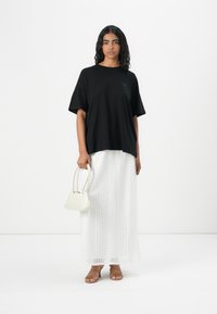 Sort oversized t-shirt med korte ærmer, parret med en lang hvid nederdel med hulmønster. Tilbehøret inkluderer en lille hvid håndtaske.