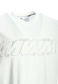 Camiseta de algodón blanca con un logo bordado "MWM" en un diseño texturizado y en relieve, con bordes deshilachados y cuello redondo.