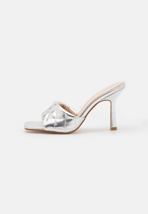 Srebrne sandały na wysokim obcasie z pikowaną metaliczną cholewką, otwarty przód oraz smukły, błyszczący obcas w stylu stiletto. Płaska podeszwa.