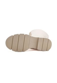 Suola beige di un stivale bianco con morsetti in gomma texturizzata su un design di battistrada piatto e segmentato.