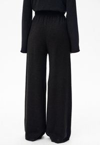 Czarne szerokie spodnie z elastycznym pasem, wykonane z teksturowanego materiału, który odbija światło. Posiadają długie, dopasowane rękawy w talii.