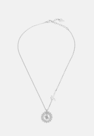 Collier chaîne argenté avec un pendentif circulaire en cristal et un petit charm "Guess" en cursive sur fond blanc.