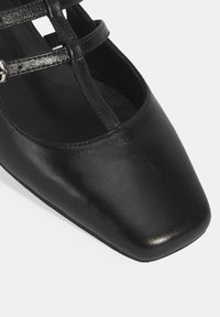 Chaussure noire en cuir à bout carré avec des fines brides croisées et une texture lisse. Présente un design élégant adapté à diverses occasions.