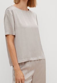 Top corto e largo in morbido satin beige. Collo rotondo, texture liscia e orlo dritto. Abbinato a pantaloni leggeri coordinati.