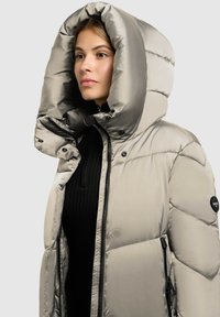 Gepolsterte Jacke in Metallic-Silber mit übergroßer Kapuze. Mit Reißverschluss vorne, schwarzer gerippter Basisschicht darunter und Logoschriftzug auf dem Ärmel.