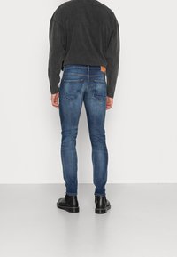 Modré úzké džíny s mírně zvýšeným pasem, pěti kapsami a koženou nášivkou na zadní straně. Dokončeno tmavě modrou košilí s dlouhým rukávem a černými botami.