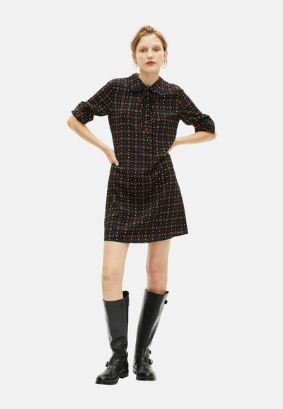 Czarna sukienka z krótkimi, podwiniętymi rękawami, zapinana na guziki, z kolorowymi, okrągłymi wzorami. Noszona z czarnymi kozakami do kolan.