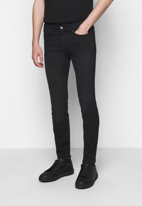 Černé slim-fit džíny vyrobené z denimu, se přední kapsou, decentním prošíváním a hladkým povrchem. V kombinaci s černými teniskami.