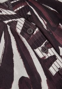 Skjorta med knappfront i ett djärvt abstrakt mönster i mörk lila och vitt, tillverkad av mjukt tyg, med synlig sömnad och mörka knappar.