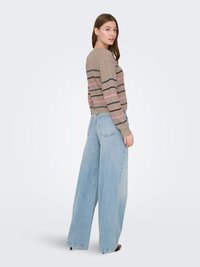 Pull en maille beige avec des rayures horizontales en bleu foncé, marron et rose ; associé à un jean large bleu clair. Texture lisse, coupe décontractée.