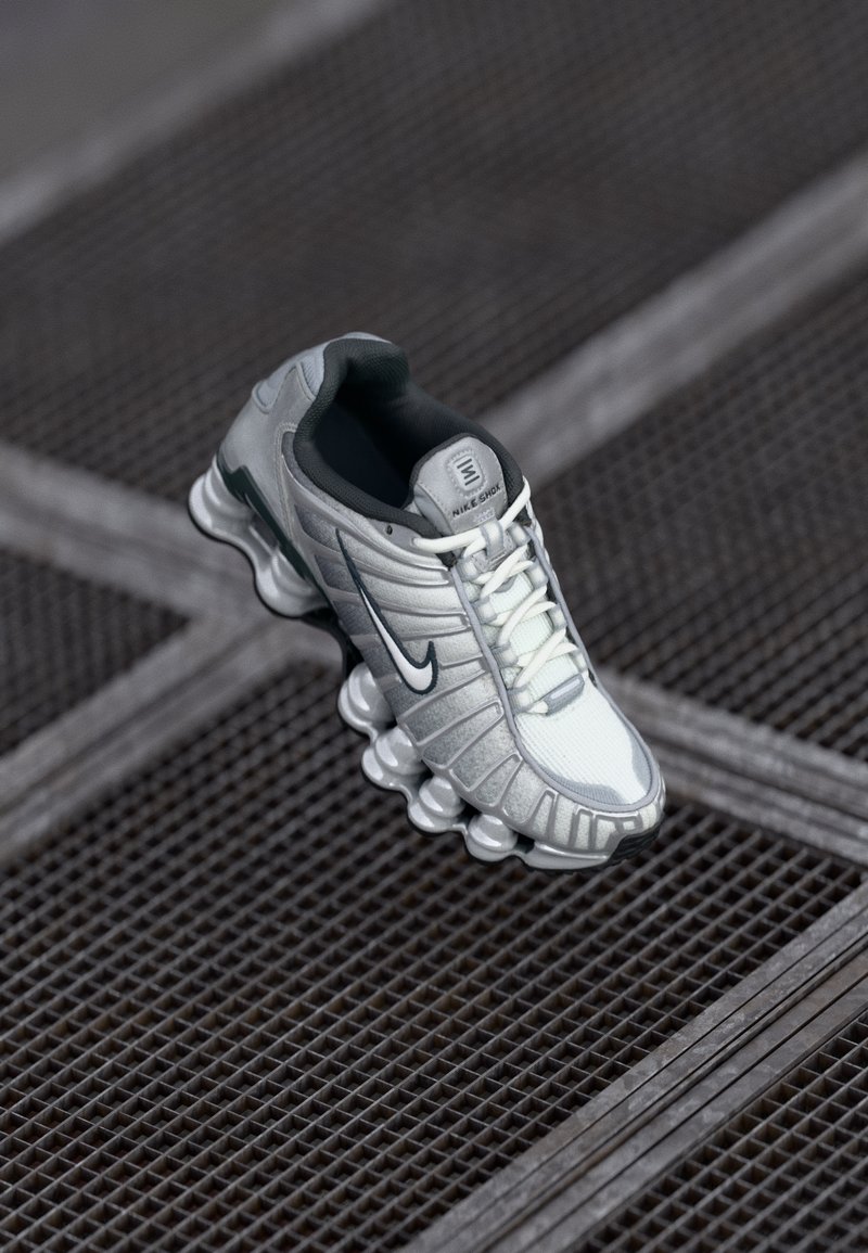 Szare i białe trampki Nike z siateczkową i syntetyczną cholewką, zaokrąglona podeszwa z wyraźnymi segmentami amortyzacyjnymi oraz ciemnoszarymi akcentami.