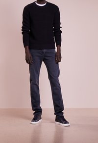 Suéter de punto oscuro con textura acanalada, combinado con jeans oscuros. El calzado consiste en zapatillas de cuero negras con suela blanca.