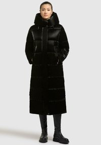 Cappotto lungo nero imbottito con colletto alto, design a righe orizzontali, chiusura frontale con zip e tasche laterali abbinato a stivali neri al ginocchio.