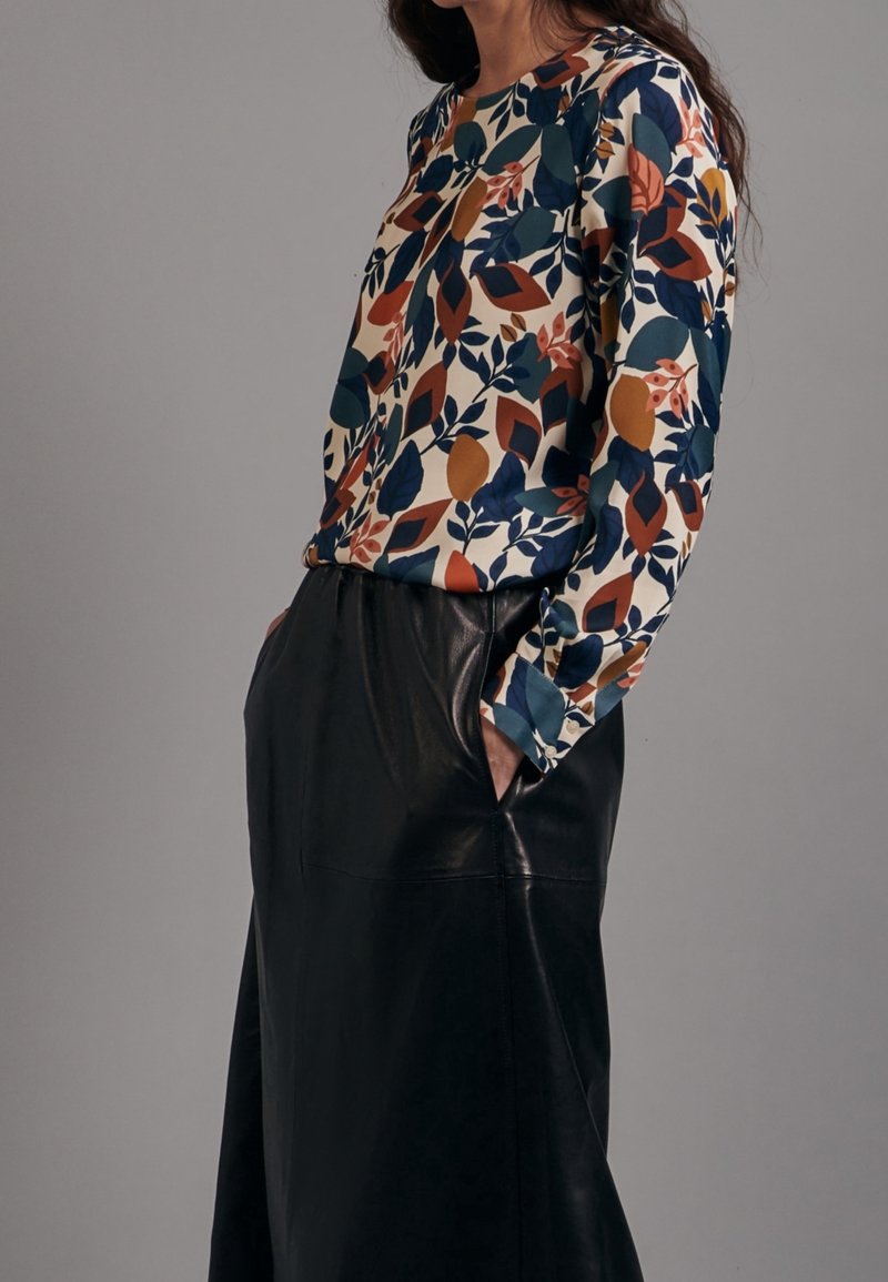 Blouse à manches longues présentant un motif floral coloré en bleu, orange et crème, associée à une jupe en cuir noire taille haute.