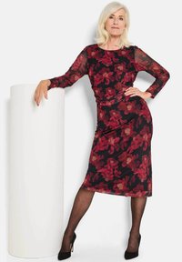 Langärmliges, eng anliegendes Kleid mit schwarzem Grund und roten Blumenmustern. Transparente Mesh-Ärmel und Midi-Länge, ergänzt durch schwarze Absätze.