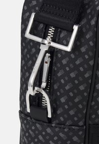 Black bag hardware features a silver zipper and clip with a textured surface, showcasing geometric patterns in a matte finish.