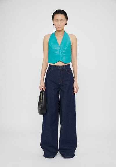 Sätimee türkiissinine crop top, mis on valmistatud läikivast materjalist, kombineerituna kõrge vöökoht ja laiad tumedad teksapüksid. Mudel hoiab käes musta käekotti.