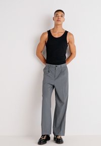 Débardeur noir, pantalon gris cintré avec des plis, et chaussures à plateforme noires avec un accent imprimé léopard. Texture de tissu lisse, design ajusté.