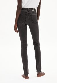 Pantalones vaqueros ajustados negros hechos de denim. Tienen una cintura alta, bolsillos traseros y costuras en contraste. La tela tiene una textura suave.