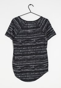 Top de manga corta en blanco y negro con un patrón de rayas texturizado, escote redondeado y dobladillo curvado. Cuelga de un gancho negro.