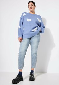 Modrý vlněný svetr s bílými vzory srdce, doplněný světle modrými texturovanými džíny a černými platformovými botami se stříbrnými detaily.