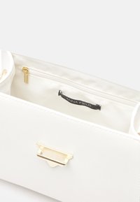 Biała skórzana torba o teksturowanym wykończeniu, z zapięciem w kolorze złota i wewnętrzną kieszenią na zamek. Podszewka z gładkiego materiału i metka z logo.