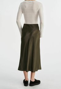 Miętowa, satynowa spódnica midi w kolorze oliwkowym zestawiona z dopasowanym białym, prążkowanym topem z długim rękawem oraz czarnymi trampkami na platformie, widok z tyłu.