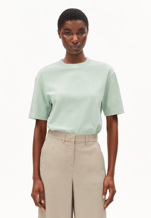 Lichtgroen katoenen T-shirt met korte mouwen, ronde hals en subtiele logodetail. Gecombineerd met beige, hooggetailleerde broek.