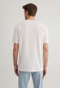 Back view of a plain white cotton t-shirt with short sleeves, crew neck, and relaxed fit, paired with light blue denim jeans.