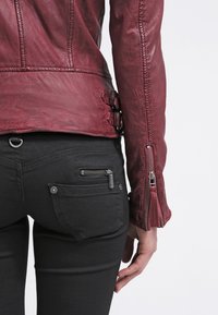 Rode leren jas met een aansluitend ontwerp, een horizontale naad ter hoogte van de taille en ritsmanchetten. Zwarte broek met ritssluitingen op de zakken en een gestructureerde stof.