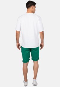 T-shirt bianca in cotone a maniche corte, abbinata a pantaloni corti verdi. I pantaloni corti sono arrotolati all'orlo. Calzature sono sneakers bianche.