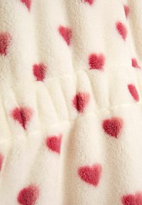 Valge fliiskangas roosa südame mustriga; pehme tekstuur ja volangdetail, luues hubase välimuse.