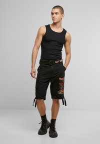 Svart singlet, cargo shorts med grafisk print og lommer, innsnevret ved beina, kombinert med svarte militærstøvler.