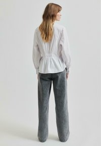 Camicia bianca con dettagli arricciati sul retro, abbinata a pantaloni larghi grigi in un tessuto morbido e testurizzato.