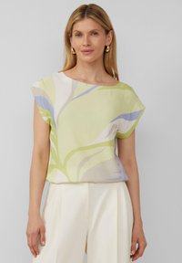 Kurzärmlige Bluse mit Floralprint in Hellgrün, mit sanften blauen und weißen Akzenten. Das Material wirkt leicht und hat eine glatte Textur.
