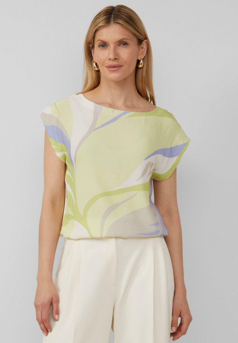 Kurzärmlige Bluse mit Floralprint in Hellgrün, mit sanften blauen und weißen Akzenten. Das Material wirkt leicht und hat eine glatte Textur.