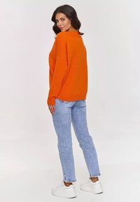 Pomarańczowy sweter z dzianiny o luźnym kroju, z prążkowanymi mankietami i dołem. Połączony z jasnoniebieskimi dżinsami i białymi sneakersami.