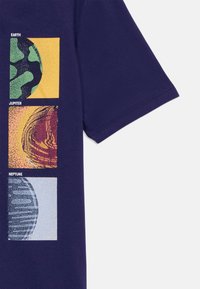 T-shirt en coton bleu marine arborant trois impressions en bloc de la Terre, de Jupiter et de Neptune, chacune avec des couleurs et des textures distinctes.