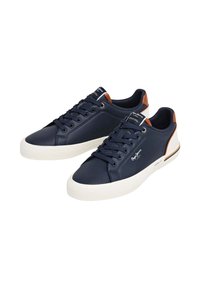 Zapatillas deportivas azul marino con parte superior texturizada, suela de goma blanca y detalles en cuero marrón en el talón. Presentan cordones redondos y detalle de logo.